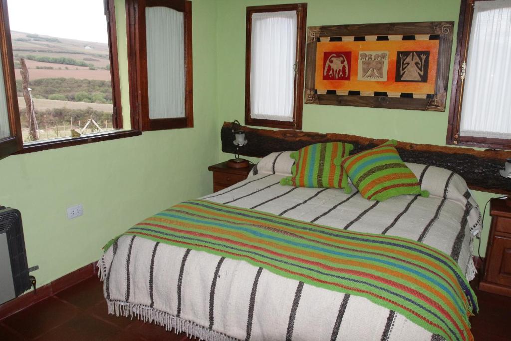 1 dormitorio con 1 cama con manta a rayas y ventanas en Villa Rural San Miguel de la Loma en Tafí del Valle