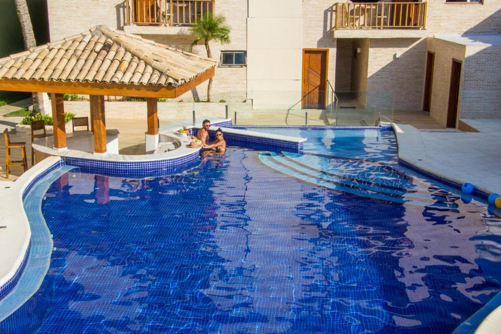 dos personas sentadas en una gran piscina azul en Strand Hotel Guarujá Frente Mar, en Guarujá