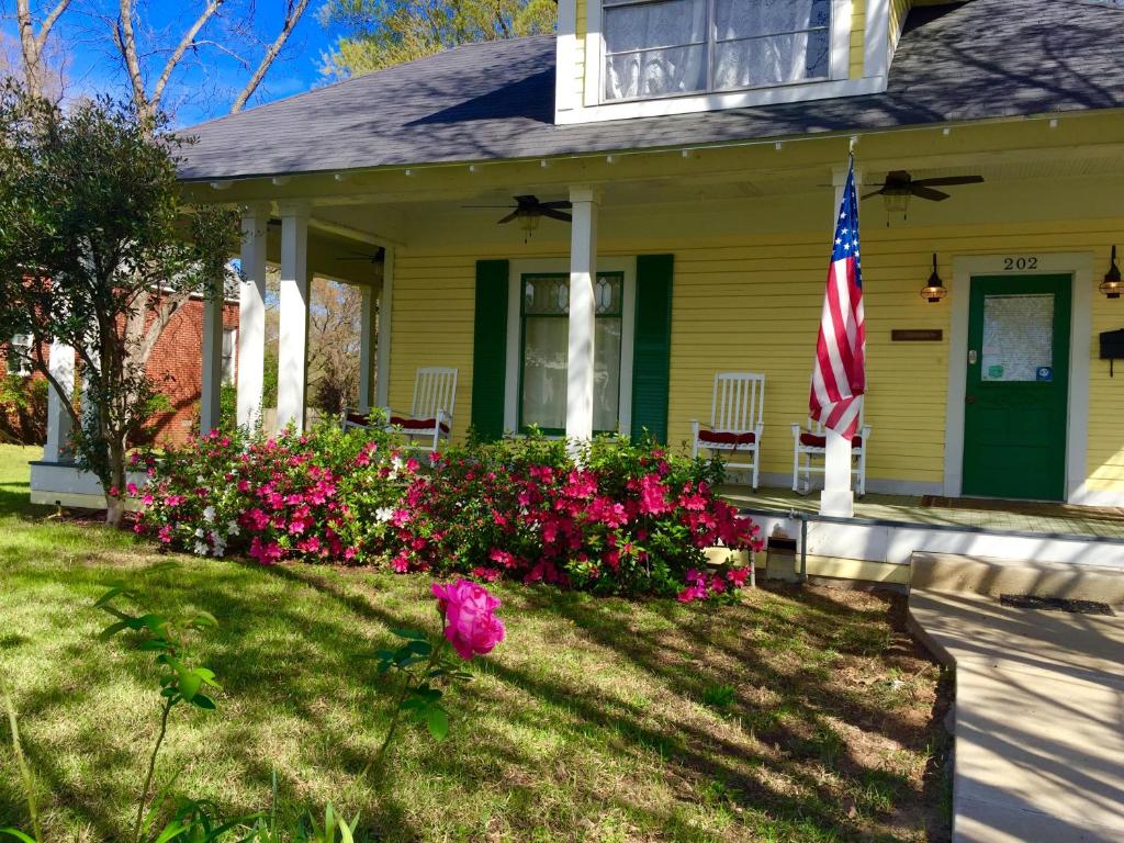 a yellow house with a flag and flowers in the yard at Brooks House Suites in Mineola