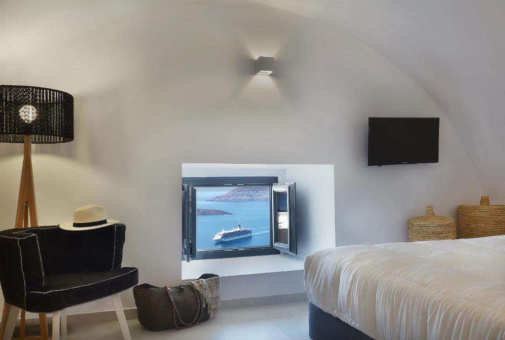 um quarto com uma cama, uma televisão e uma cadeira em Callia Caves - Adults Only em Fira