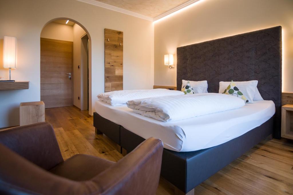 a bedroom with a large bed and a chair at Hotel Garni Vigilhof in Lana