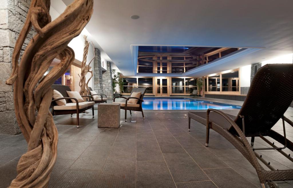 a swimming pool with chairs and a table and a building at CGH Résidences & Spas Les Chalets de Jouvence in Les Carroz d'Araches