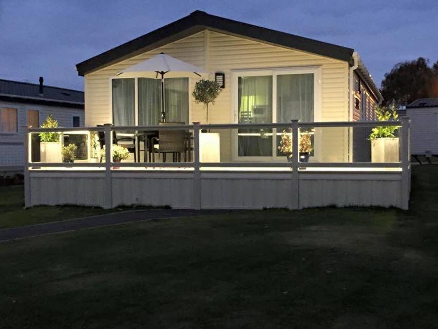 a house with a wooden deck with an umbrella at Highfields Holiday Park Clacton in Clacton-on-Sea