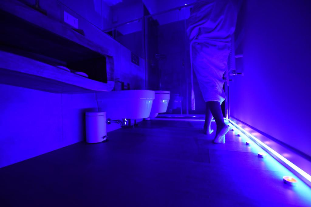 マテーラにあるNicola's Luxury Roomsの紫色の照明付き浴室に立つ者