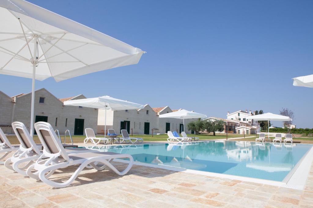 einen Pool mit weißen Stühlen und einem Sonnenschirm in der Unterkunft Agrumare Farm Holiday in Marina di Pisticci
