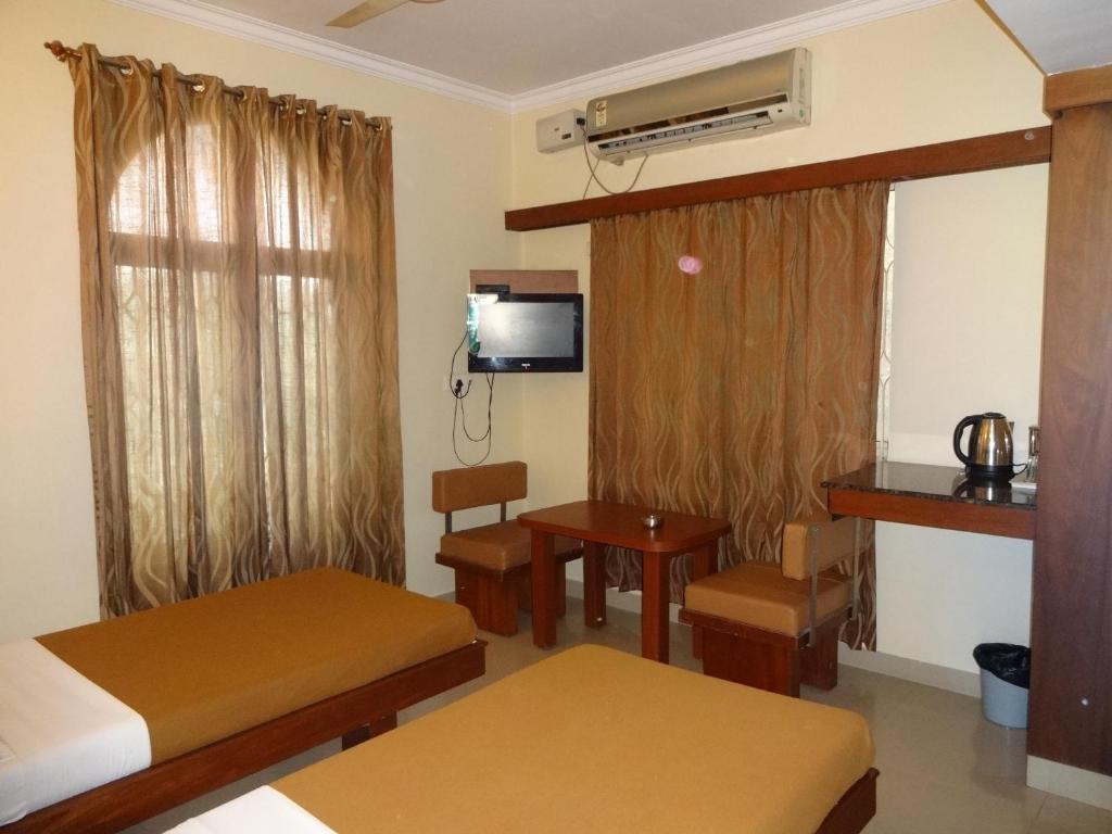 a room with two beds and a table and a television at Sheetal Residency in Bangalore