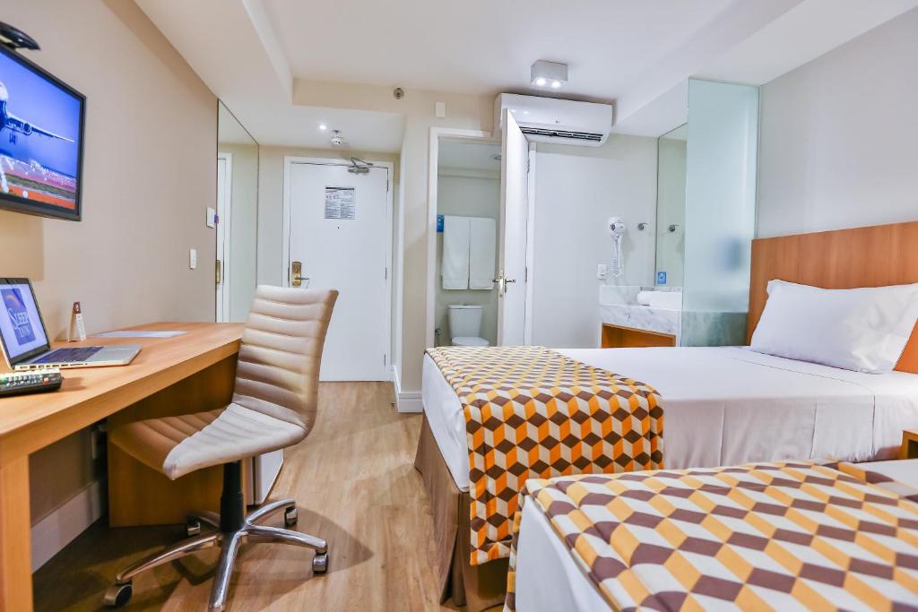 a room with two beds and a desk with a computer at Sleep Inn Aeroporto de Guarulhos - São Paulo in Guarulhos