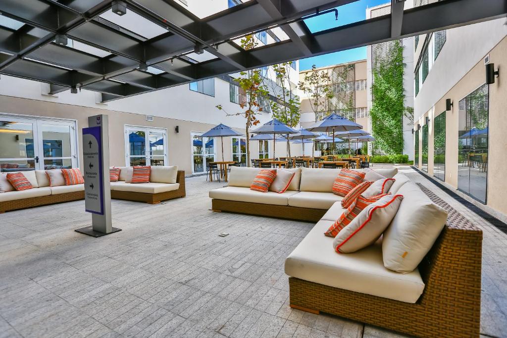 a patio with couches and tables and blue umbrellas at Sleep Inn Aeroporto de Guarulhos - São Paulo in Guarulhos