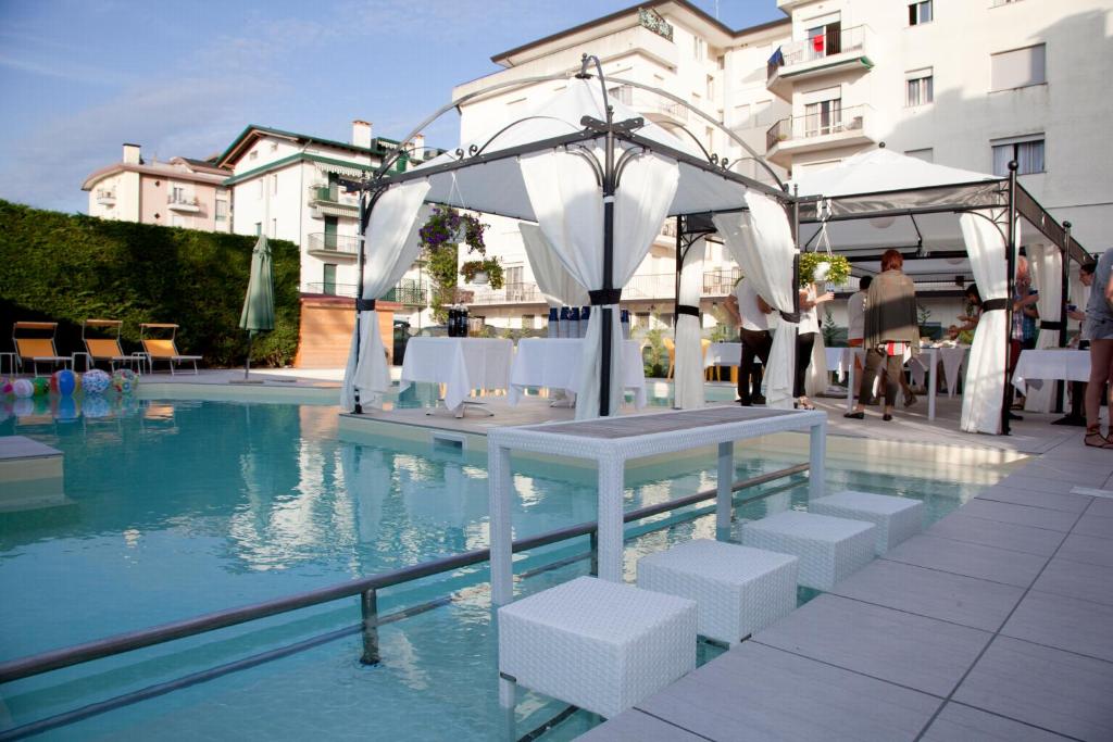 una piscina con tavolo e sedie bianche accanto ad alcune acque di Ute Hotel a Lido di Jesolo