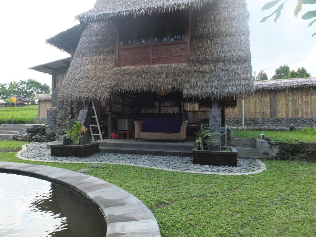 ein Haus mit einem Strohdach und einem Pool in der Unterkunft Uma Nirmala Aling-Aling in Singaraja