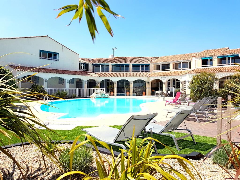 a swimming pool with lounge chairs in front of a building at Hôtel Restaurant Le Grand Large - Face à la plage - Ile de Ré in Rivedoux-Plage