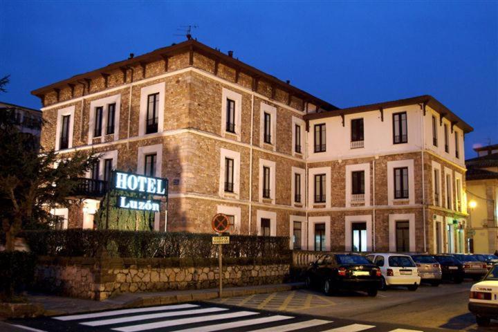 duży ceglany budynek z samochodami zaparkowanymi przed nim w obiekcie Hotel Luzon w mieście San Vicente de la Barquera