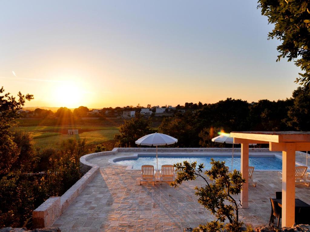 a pool with chairs and umbrellas at sunset at B&B Lamie Di Olimpia in Locorotondo