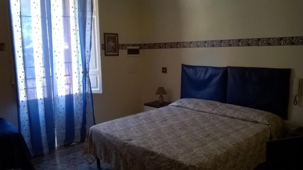 1 dormitorio con 1 cama con cortinas azules y ventana en Casetta al Centro, en Trapani