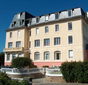 un grand bâtiment blanc avec un toit noir dans l'établissement Residence des Bains, à Carantec