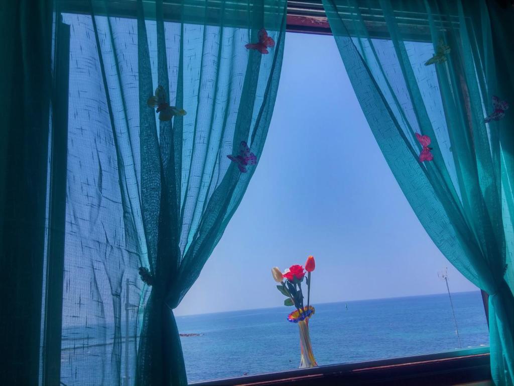 a window with a view of the ocean with a bouquet of flowers at 777 Beach Guesthouse in Paphos City