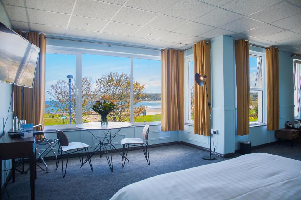 a room with a bed, chair, table and a window at Marine Hotel Ballycastle in Ballycastle