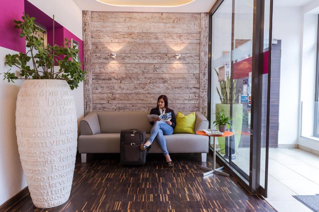 a woman sitting on a couch with a suitcase at Hotel Arooma in Erding