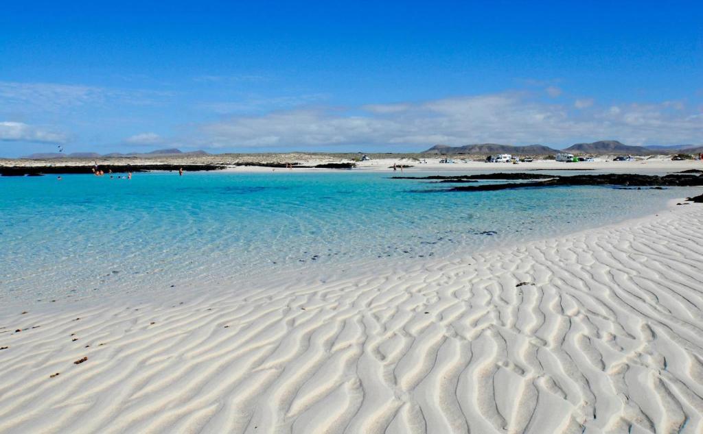 una spiaggia con acqua blu e onde nella sabbia di Casa Paradise a Cotillo