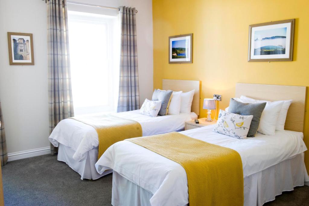 two beds in a hotel room with yellow walls at Rose and Crown Hotel in Carmarthen