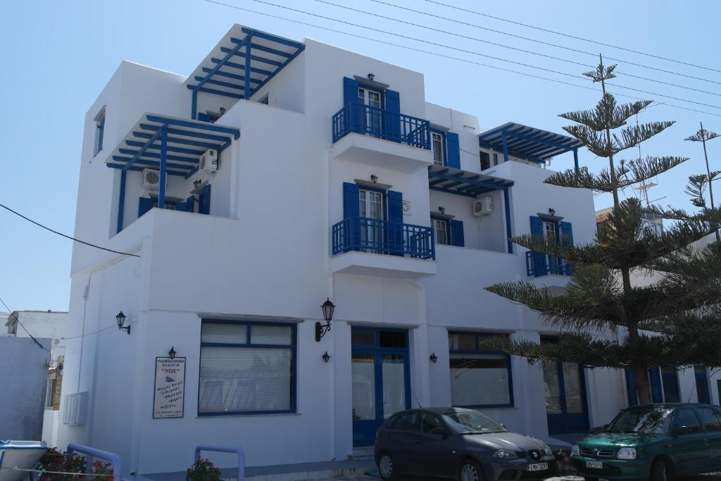un edificio blanco con ventanas azules y coches aparcados delante en Noe Rooms, en Tinos