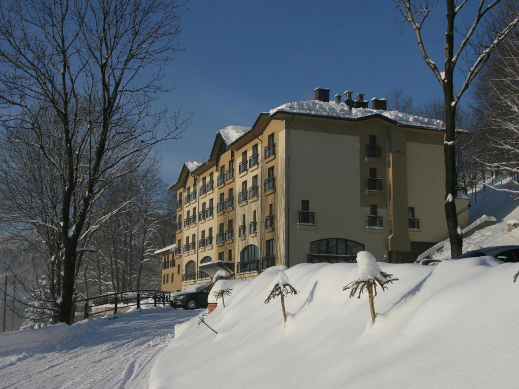 Four-story hotel building beside snow-covered path and bare trees under clear blue sky.