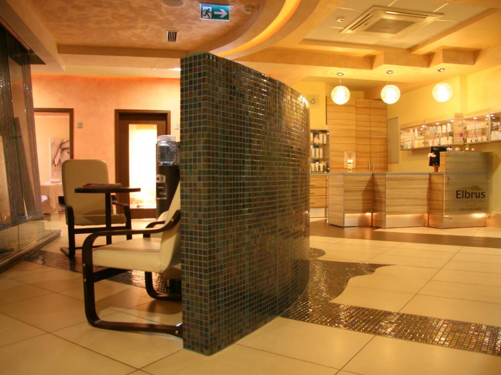 Spa reception featuring curved mosaic partition, comfortable chairs and illuminated wooden front desk.