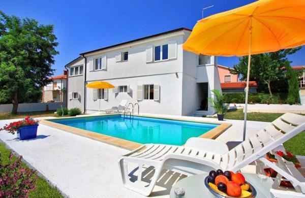 een zwembad met 2 stoelen en een parasol bij Apartment Bella in Ližnjan