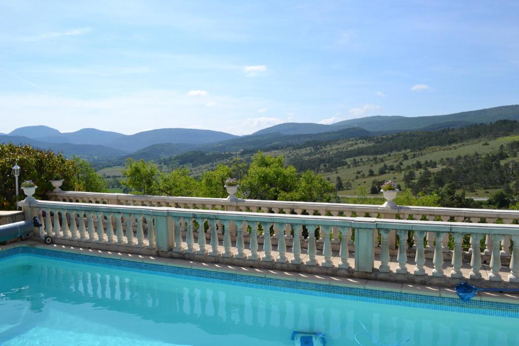 une piscine avec une clôture blanche et des montagnes en arrière-plan dans l'établissement Logis Hôtel Le Vieil Amandier, à Trigance