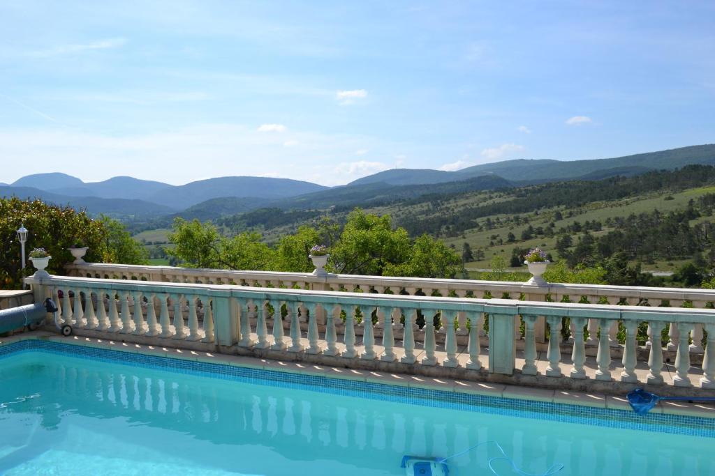 a pool with a white fence and mountains in the background at Logis Hôtel Le Vieil Amandier in Trigance