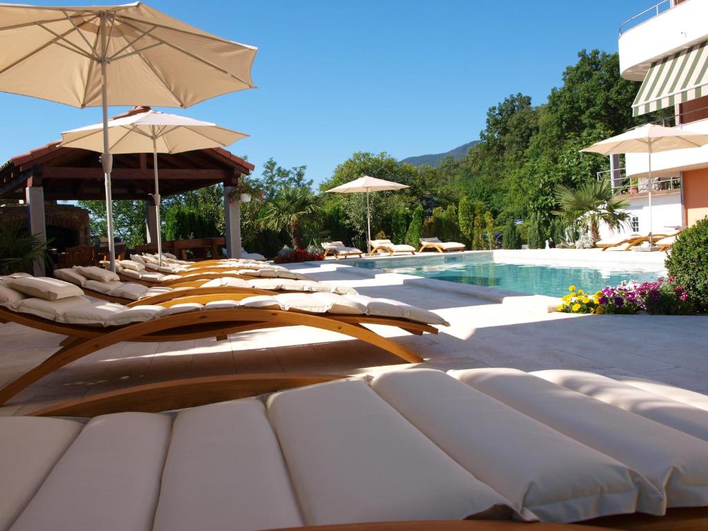 een rij ligstoelen met parasols naast een zwembad bij Apartments Villa Učka in Opatija
