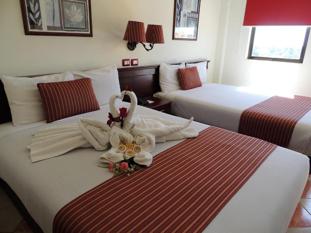 a hotel room with two beds with towels and flowers at Hotel Residencial in Mérida