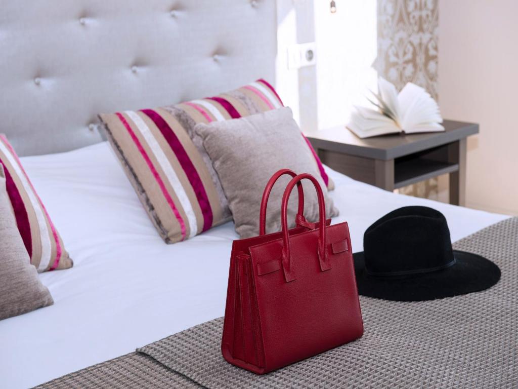 a red bag and a black hat on a bed at Hôtel Le Royal Promenade des Anglais in Nice