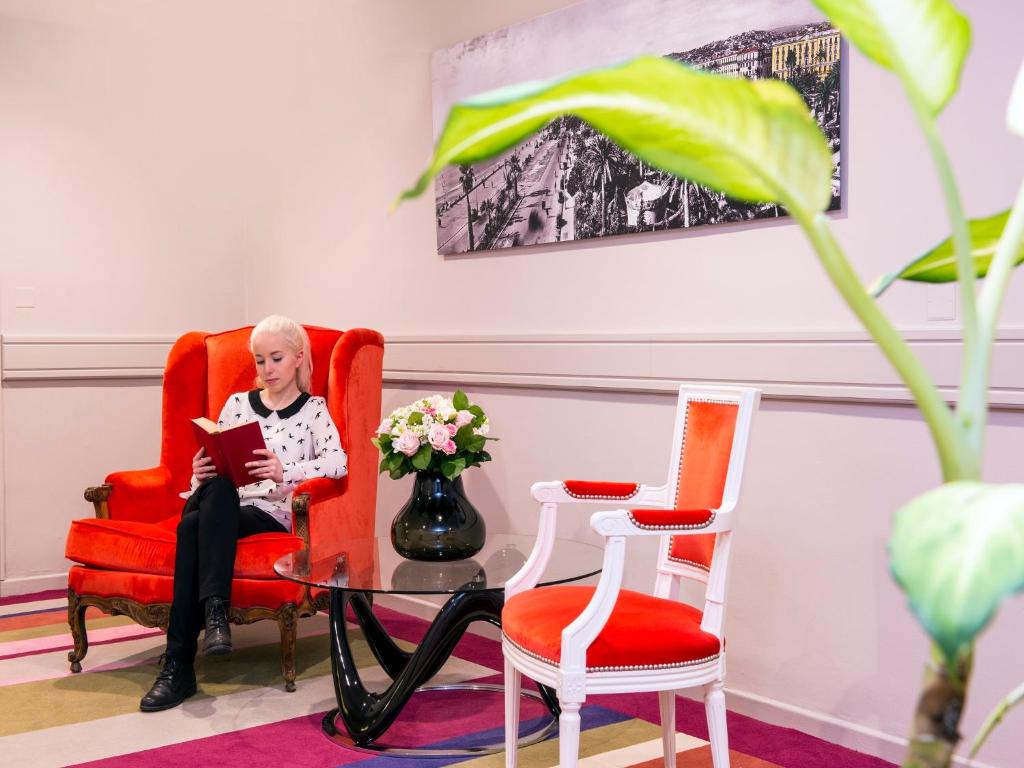 a woman sitting in a red chair reading a book at Hôtel Le Royal Promenade des Anglais in Nice