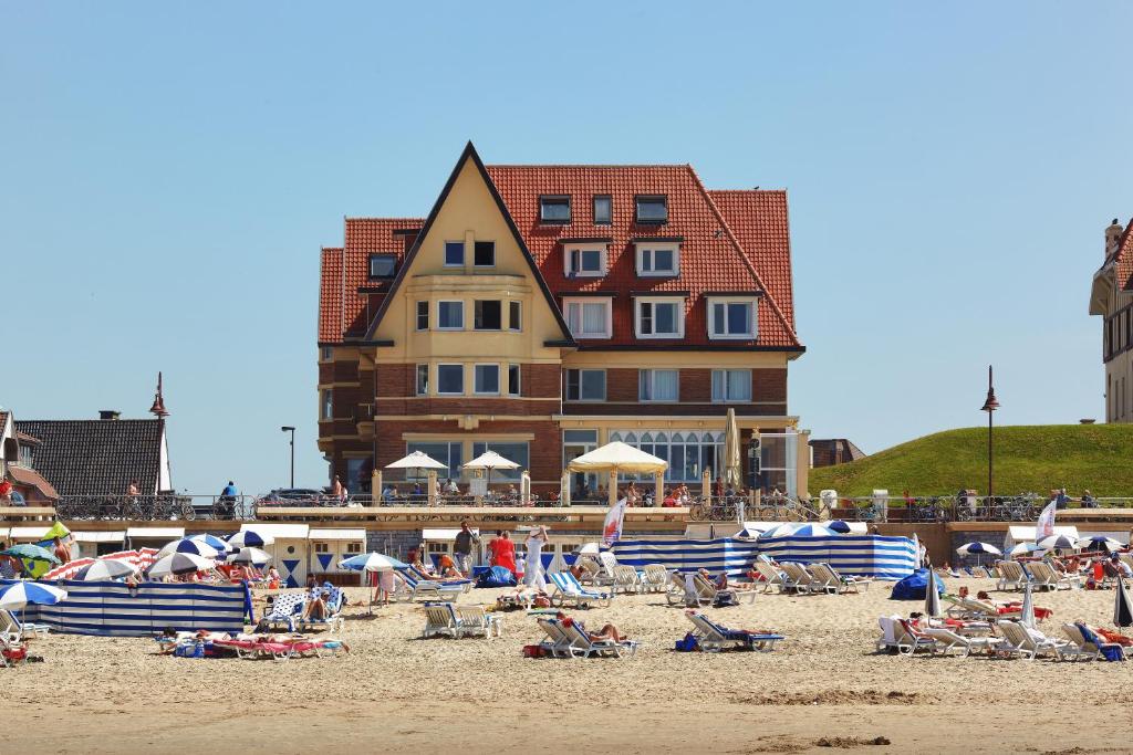 a beach with people sitting on the sand and a building at Beach Hotel in De Haan