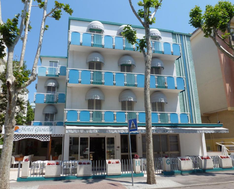 a hotel with blue balconies and palm trees at Hotel Gioiella in Rimini