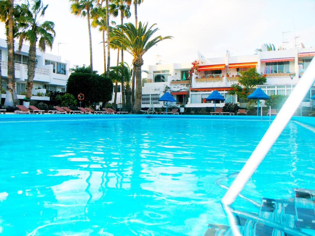 a swimming pool with palm trees and buildings in the background at Apartment Chaparral Complex in Costa Del Silencio