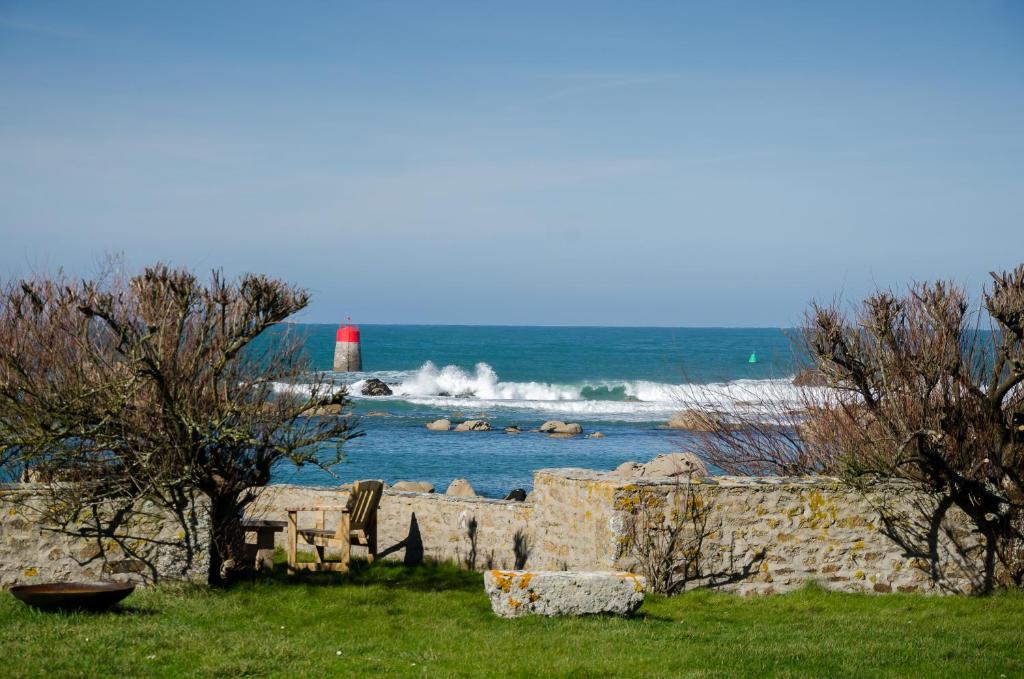 czerwona latarnia morska w wodzie z kamienną ścianą i drzewami w obiekcie Maison de La pointe w mieście Brignogan-Plages