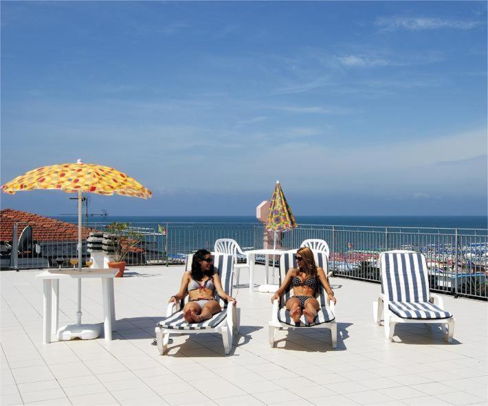 two women in bathing suits sitting in chairs on a beach at Hotel Happy in Marina di Pietrasanta