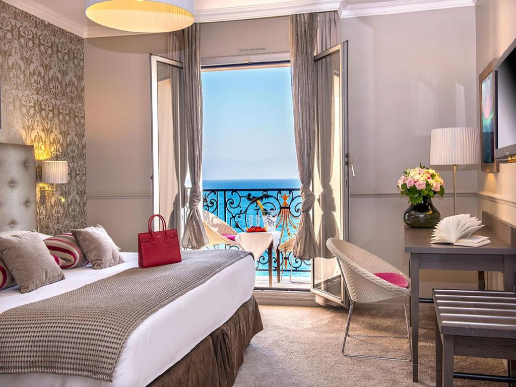 a hotel room with a bed, table and window at Hôtel Le Royal Promenade des Anglais in Nice