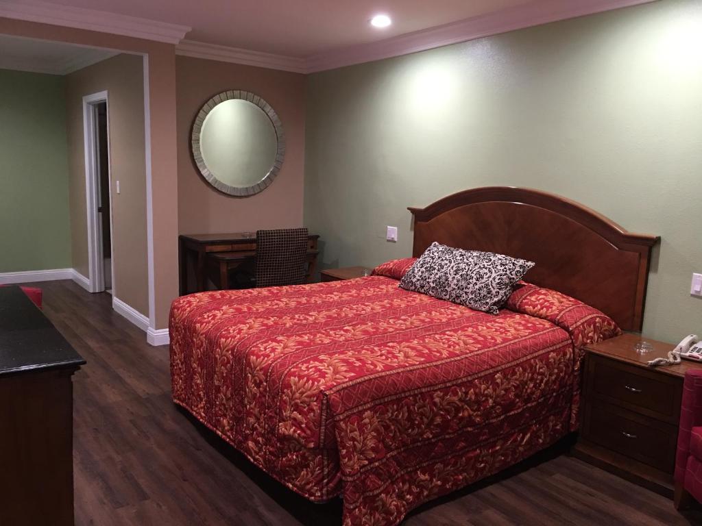 a bedroom with a bed with a red comforter and a mirror at American Inn & Suites LAX Airport in Inglewood