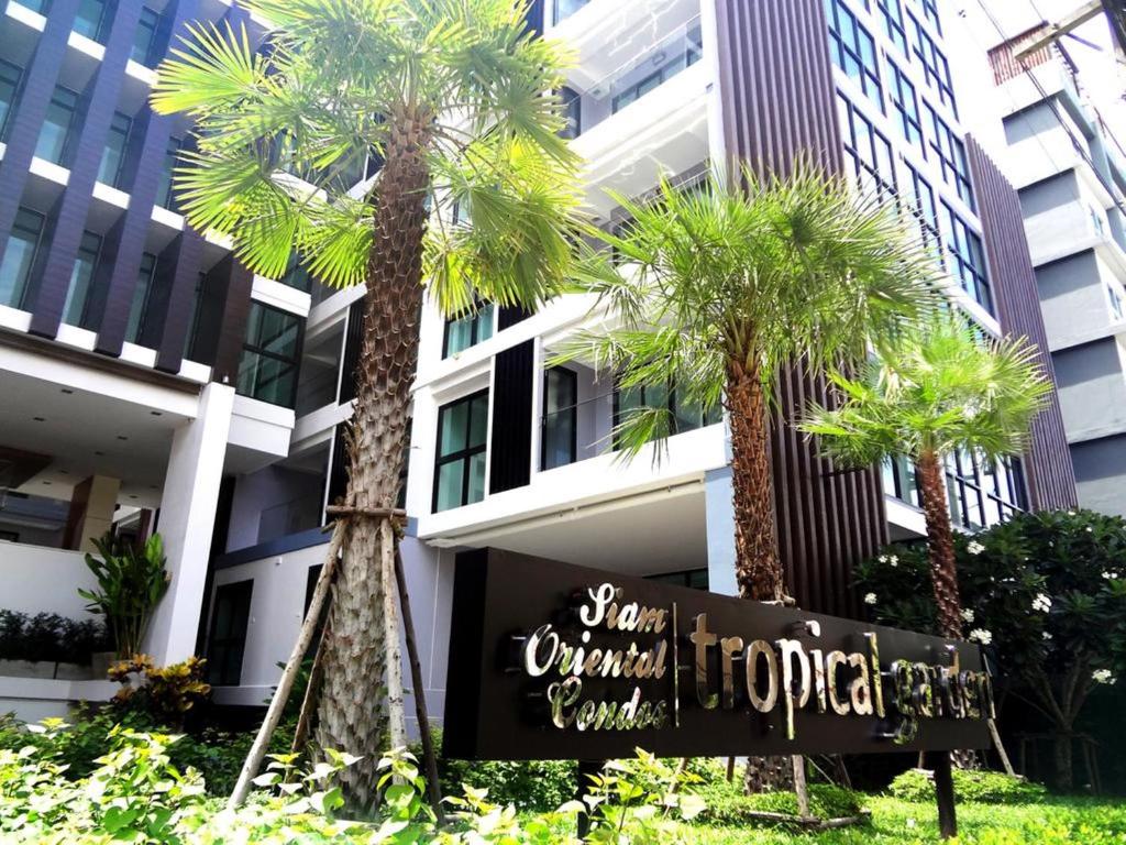 a hotel sign in front of a building with palm trees at Tropical Garden Studio in Pattaya South