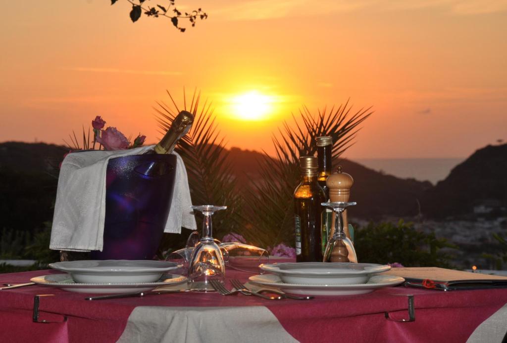 una mesa con platos y botellas de vino y la puesta de sol en Hotel Bel Tramonto, en Isquia