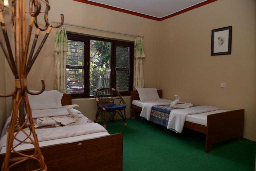a room with two beds and a chair and a window at Nepali Cottage Guest House in Pokhara
