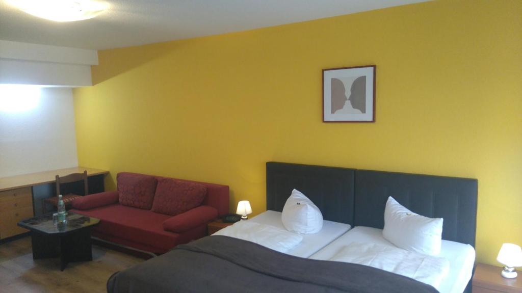 ダルムシュタットにあるホテル アーハイルガー ホフのベッドと赤い椅子が備わるホテルルームです。