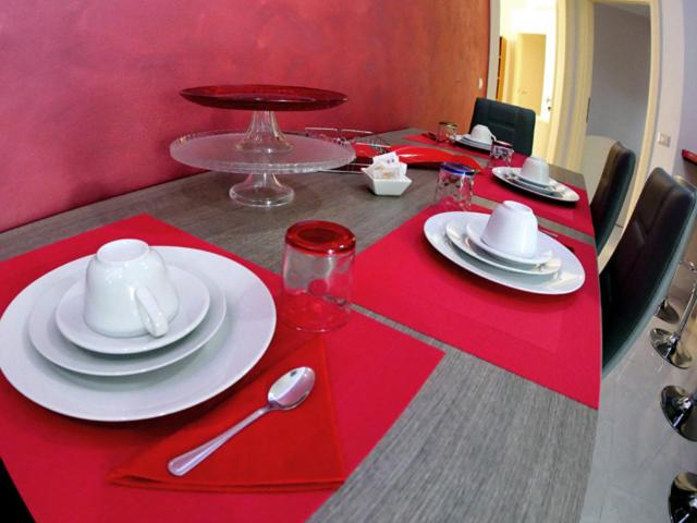 une table rouge avec des assiettes blanches et des cuillères dessus dans l'établissement Diamante dello Jonio, à Cariati