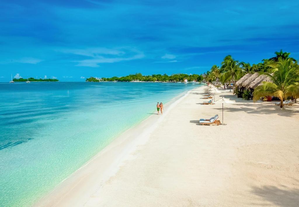 a beach with palm trees and people on it at Sandals Negril Beach All Inclusive Resort and Spa - Couples Only in Negril
