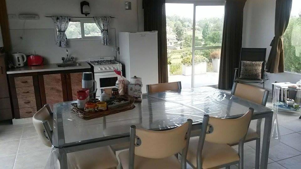 cocina con mesa de cristal con sillas y fogones en Mini Complejo El Encuentro en Sierra de los Padres