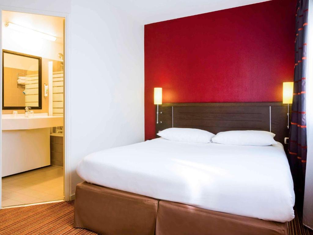 une chambre avec un grand lit blanc avec un mur rouge dans l'établissement ibis Styles Nantes Centre Place Royale, à Nantes