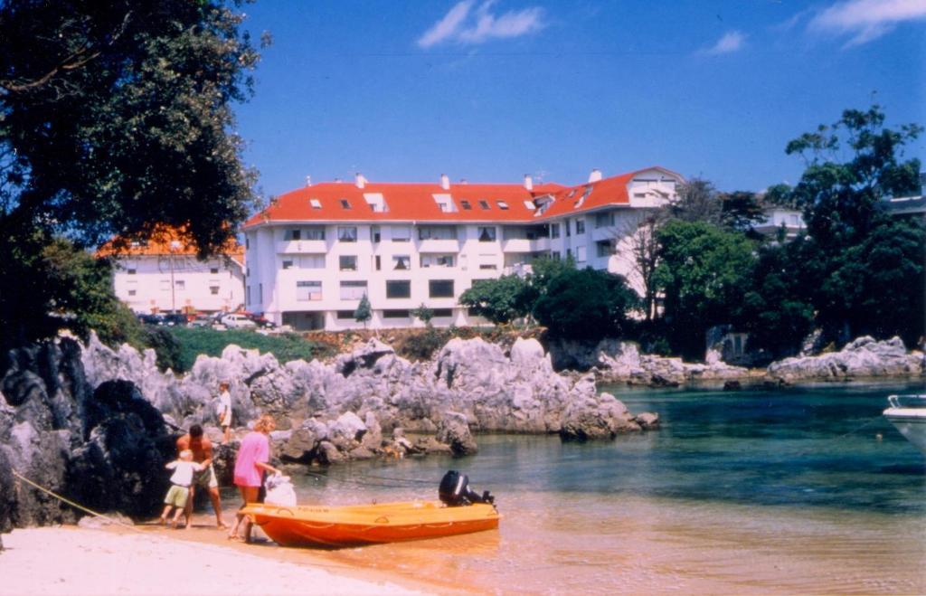 un groupe de personnes debout sur une plage avec un bateau dans l'établissement Apartamentos de la Hoz, à Isla